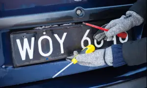Ręce w rękawiczkach odkręcają śruby tablicy rejestracyjnej.