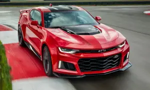 Czerwone Camaro ZL1 z czarnymi pasami na masce i dachu, pędzące po torze wyścigowym.