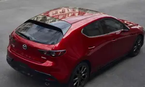 Czerwony hatchback Mazda 3 z czarnymi felgami, odbijający budynek na dachu. Wygląda elegancko, w przeciwieństwie do nudnego sedana.