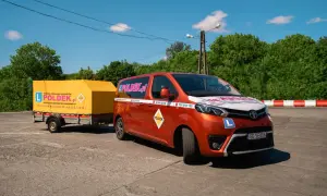 Pomarańczowy bus i żółta przyczepa z logo "POLDEK.pl" na placu manewrowym. Dowiedz się, ile kosztuje prawo jazdy E.