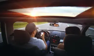 Kierowca z telefonem w ręku, zasada ograniczonego zaufania w praktyce. Słońce zachodzi, droga przed nimi.