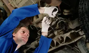 Mechanik w niebieskim kombinezonie naprawia samochód, używając klucza do dokręcenia śruby. Jego biała manszeta jest widoczna.