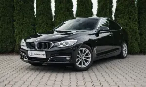 Eleganckie, czarne BMW GT lśni na tle zielonych drzew.