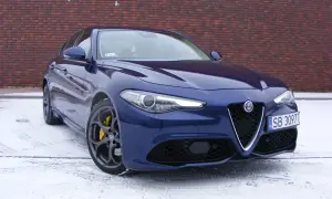 Niebieskie Alfa Romeo Giulia Veloce z żółtymi zaciskami hamulcowymi na tle ceglanej ściany, na śniegu.