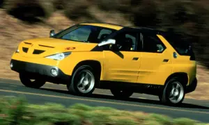 Żółty Pontiac Aztek jedzie po drodze, otoczony rozmytą zielenią i brązem.
