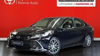 Czarny Toyota Camry 2023, lśniący na tle czerwonej ściany, prezentuje się jako pewny wybór z gwarancją.