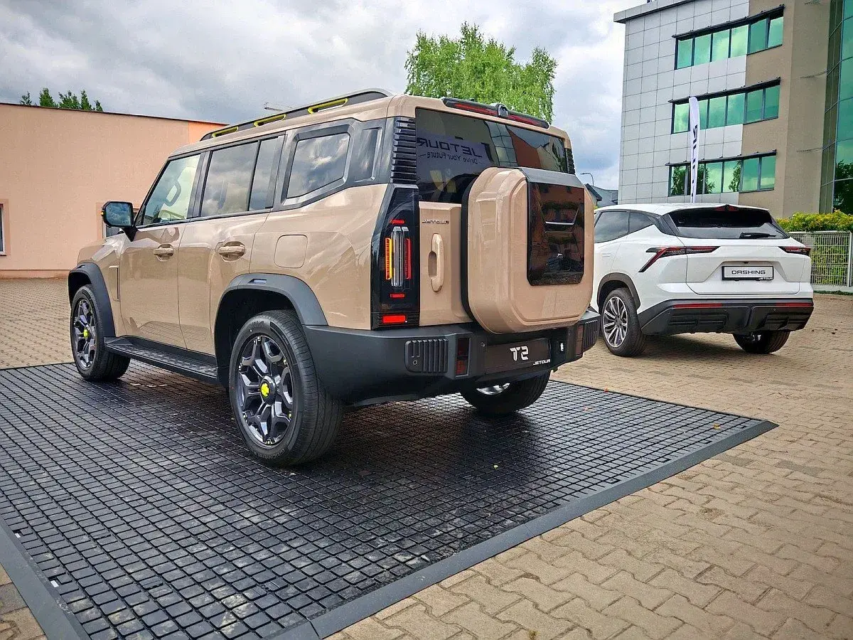 Beżowy Jetour T2 z kołem zapasowym z tyłu, obok białego SUV-a. Sprawdź Jetour T2 cena i dostępne opcje.