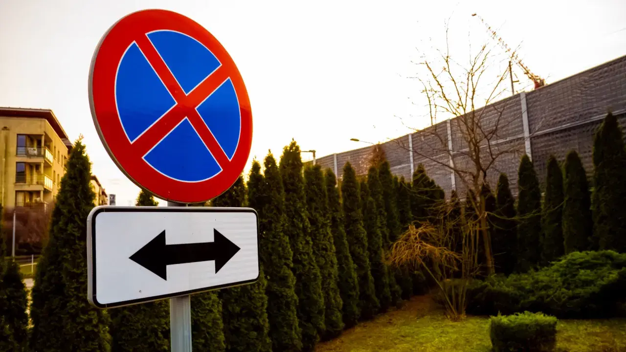 Znak zakaz parkowania z tabliczką wskazującą kierunki.