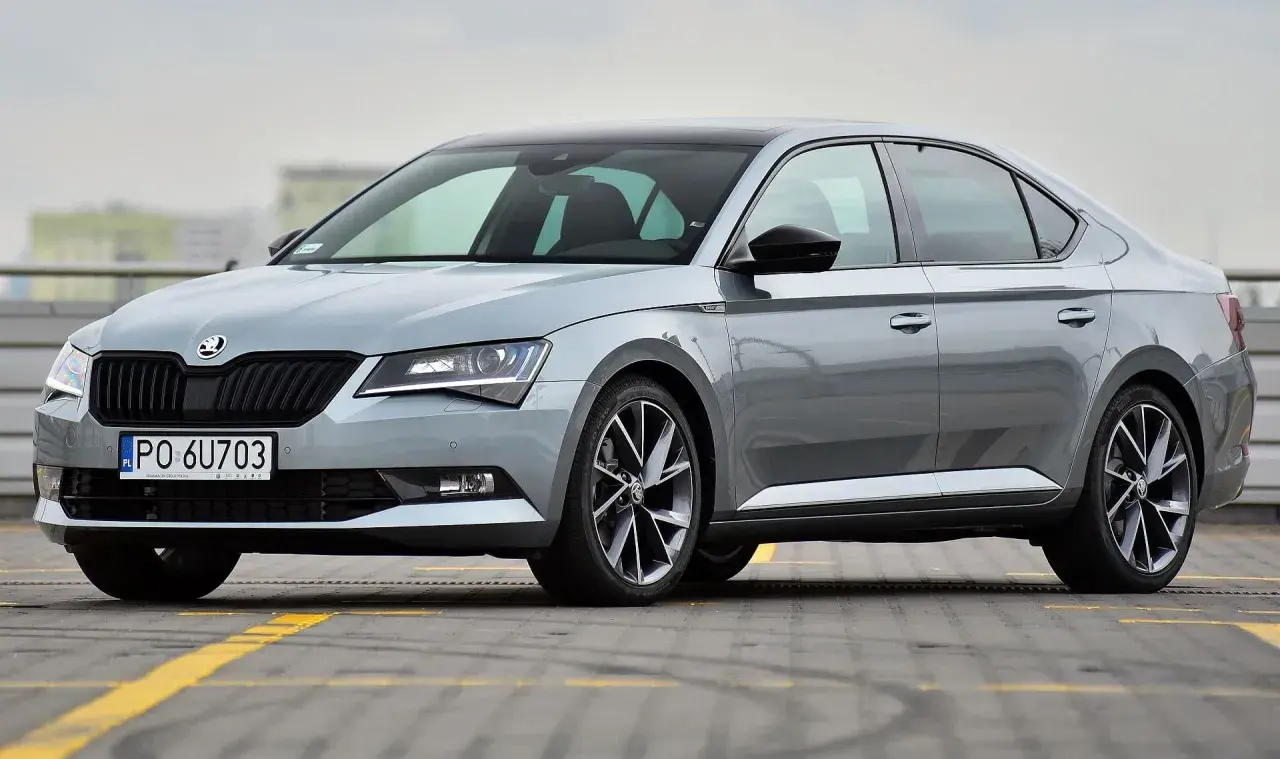 Elegancki, szary Skoda Superb 2024 z czarnym dachem i przyciemnianymi szybami, zaparkowany na parkingu.