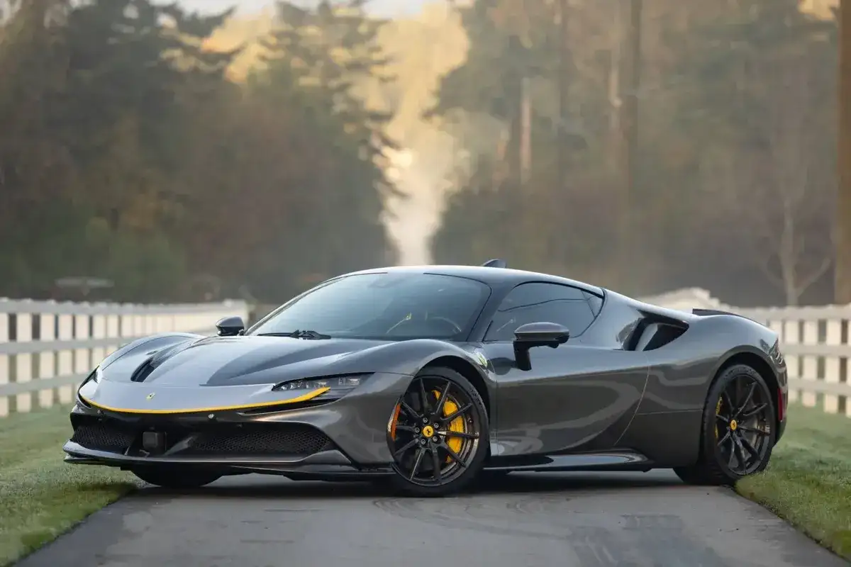 Szary Ferrari SF90 z żółtymi akcentami na tle jesiennego krajobrazu.