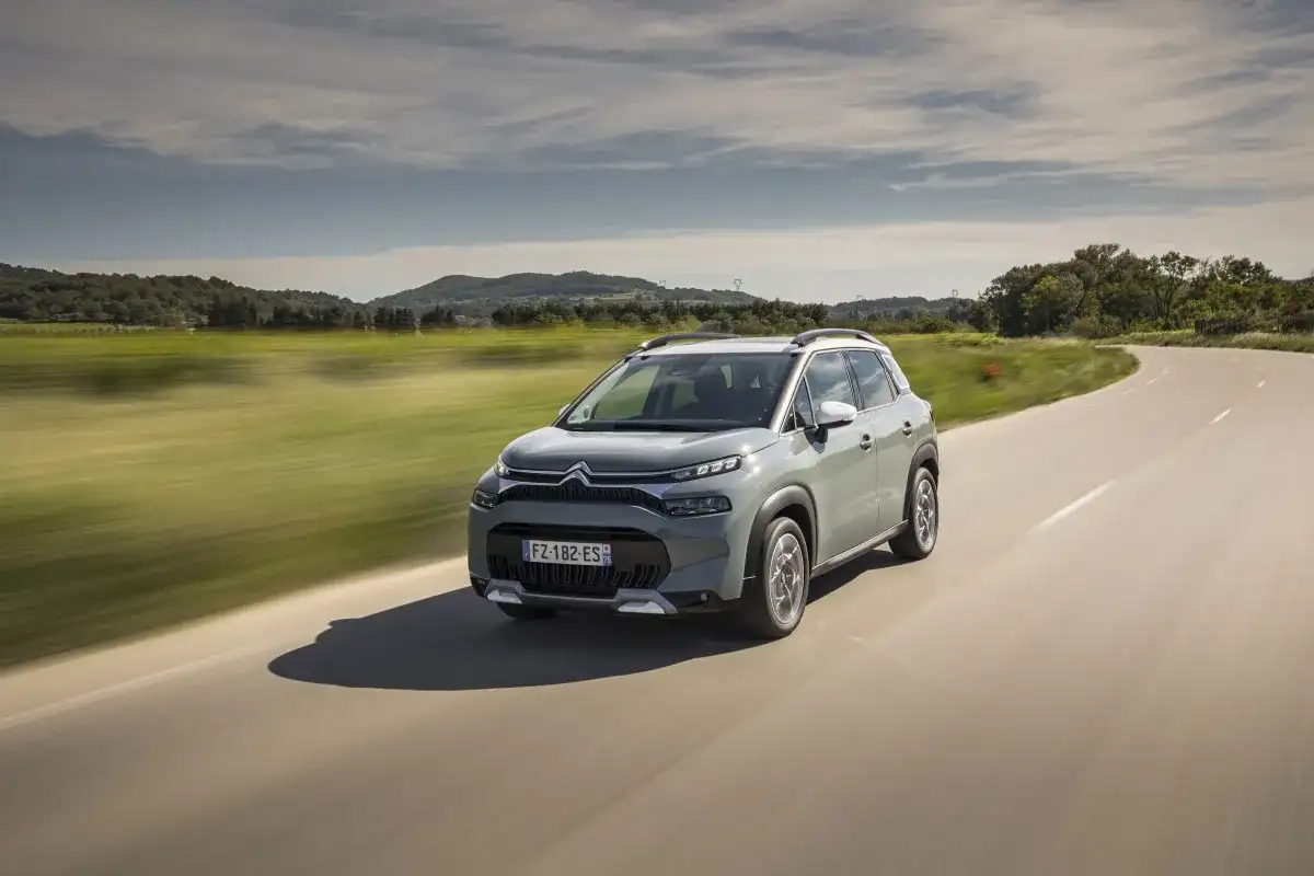 Szary Citroen C3 pokonuje zakręt na wiejskiej drodze, otoczony zielonymi polami i wzgórzami.