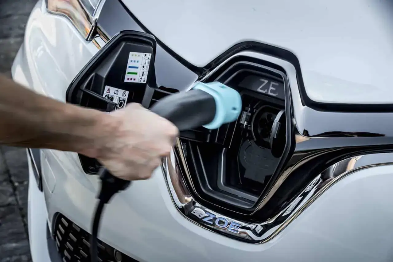 Ręka podłącza ładowarkę do samochodu elektrycznego Renault Zoe. Zbliżenie na port ładowania i logo Zoe.