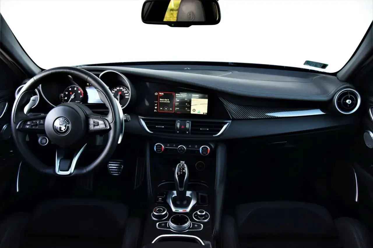 Wnętrze Alfa Romeo Giulia Veloce: kierownica, deska rozdzielcza z ekranem multimedialnym i panelem klimatyzacji, dźwignia zmiany biegów.