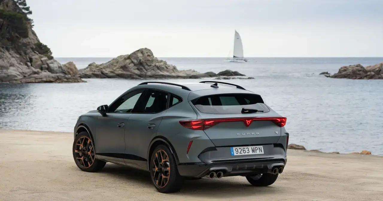 Szary Cupra Formentor z miedzianymi felgami na tle morza i skał. Sprawdź aktualną cupra formentor cena.