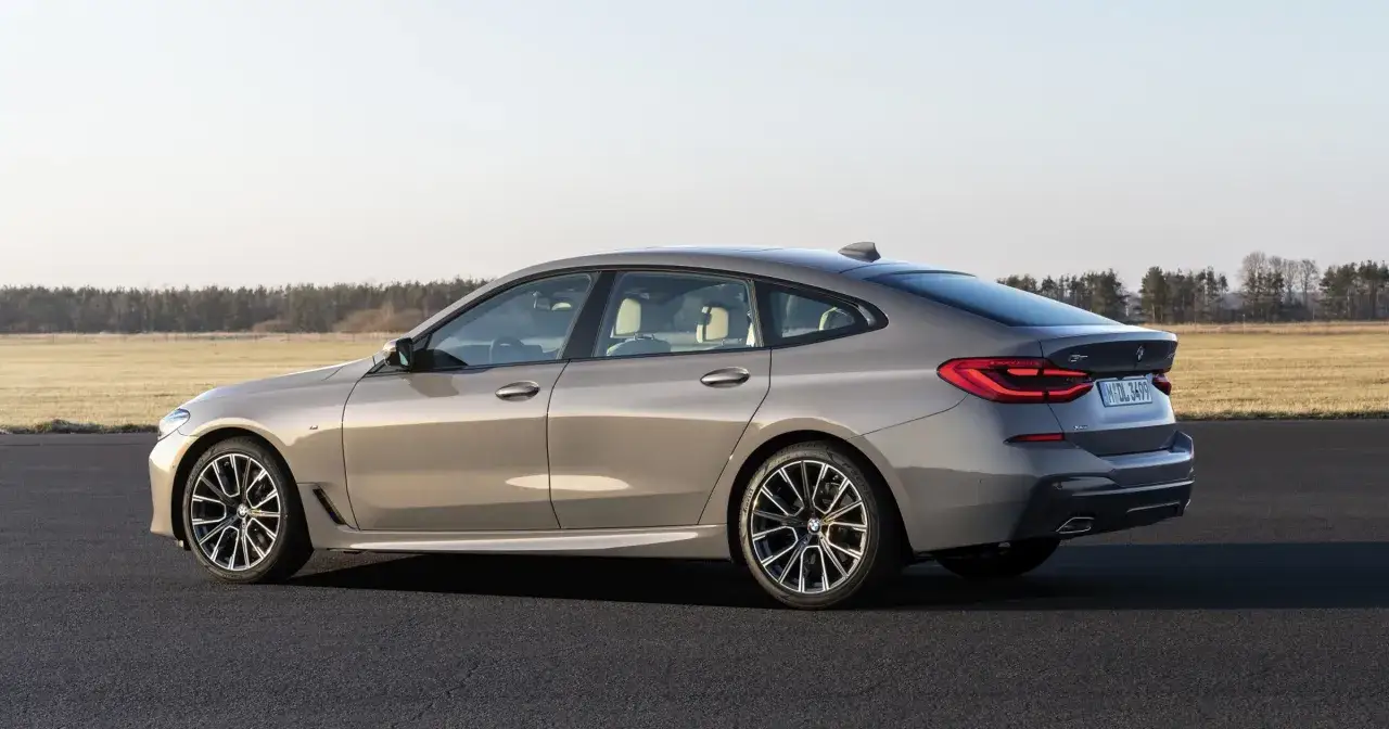 Eleganckie bmw gt w kolorze szarym, zaparkowane na asfalcie, z widokiem na pole i las w tle.