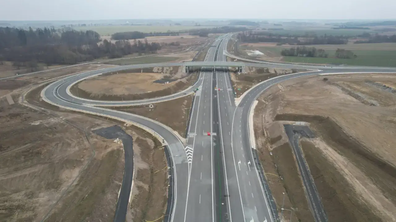 Rozbudowana autostrada A2 z wielopoziomowym węzłem drogowym, otoczona polami i lasami.