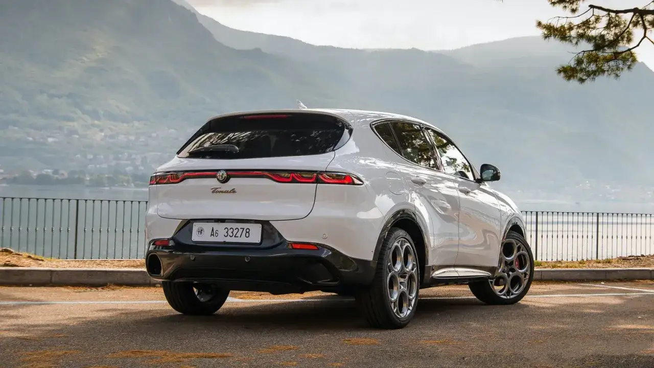 Białe Alfa Romeo Tonale z pięknymi felgami, zaparkowane nad jeziorem. Sprawdź aktualną alfa romeo tonale cena.