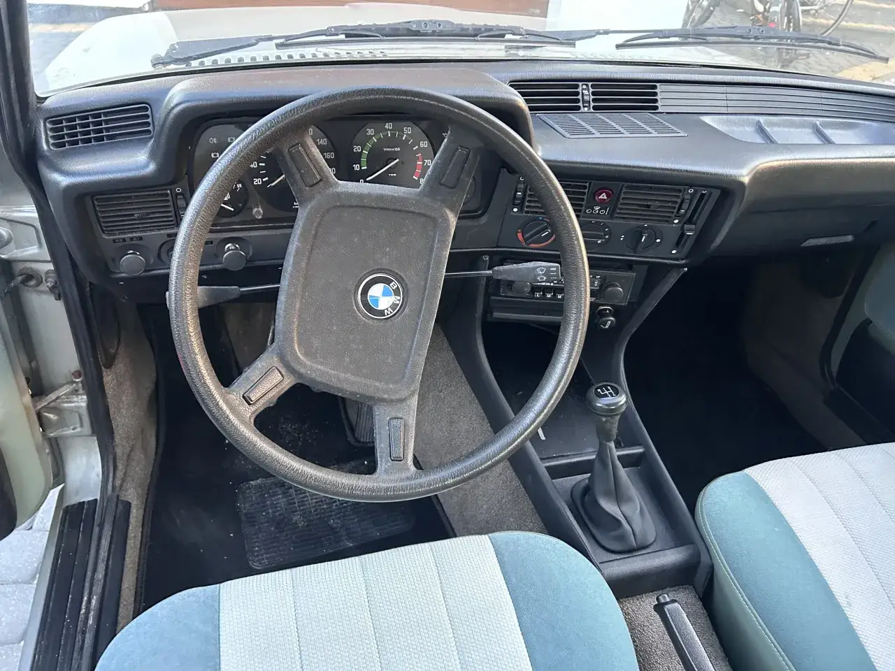 Wnętrze klasycznego BMW 318i: kierownica z logo, deska rozdzielcza z zegarami i dźwignia zmiany biegów.