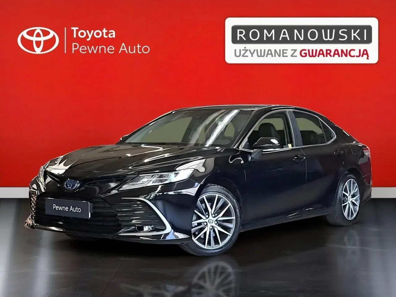 Czarny Toyota Camry 2023, lśniący na tle czerwonej ściany, prezentuje się jako pewny wybór z gwarancją.