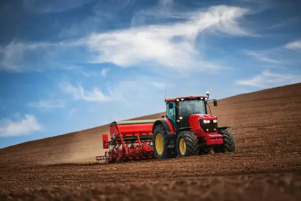 Czerwony traktor z siewnikiem orze pole. To obrazek z kategorii "prawo jazdy" kategorii T, pokazujący pracę w rolnictwie.