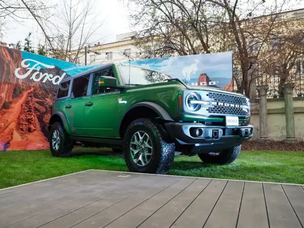Zielony Ford Bronco prezentuje się imponująco na tle krajobrazu z pustynią i logo Ford.