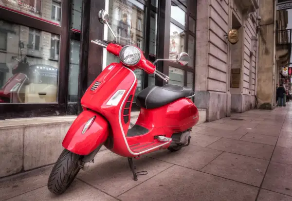 Czerwona Vespa na chodniku, marzenie o wolności i łatwym zdobyciu prawa jazdy AM za darmo.