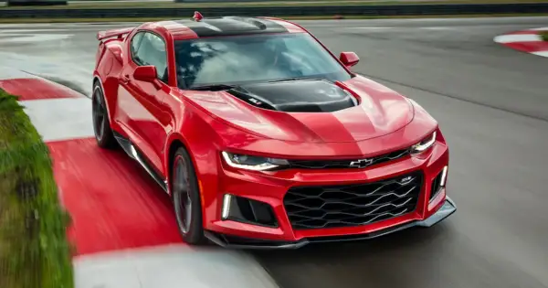 Czerwone Camaro ZL1 z czarnymi pasami na masce i dachu, pędzące po torze wyścigowym.