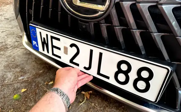 Dłoń poprawia tablicę rejestracyjną z numerem WE 2JL88.