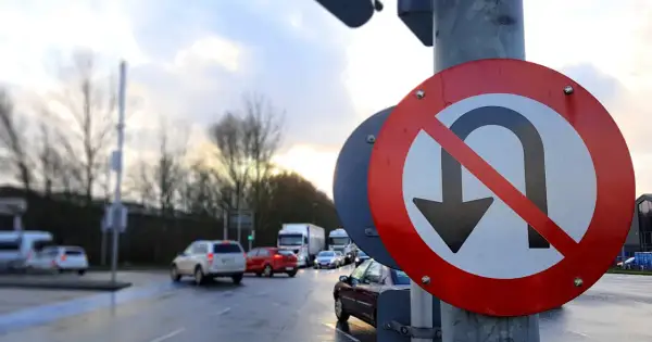 Znak drogowy zakaz zawracania na tle mokrej drogi i samochodów.