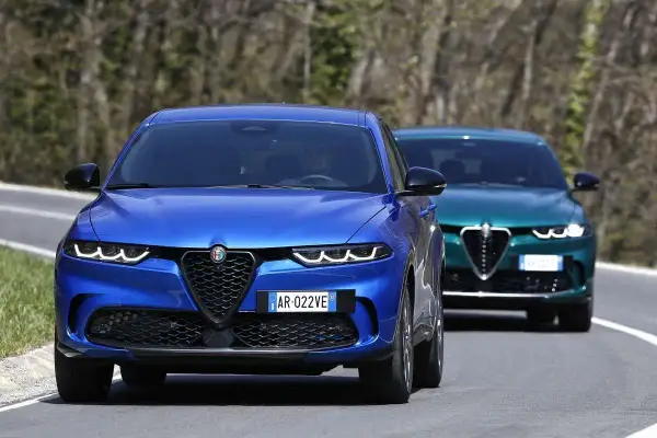 Dwa Alfa Romeo Tonale, jeden niebieski, drugi zielony, jadą drogą. Sprawdź alfa romeo tonale cena!