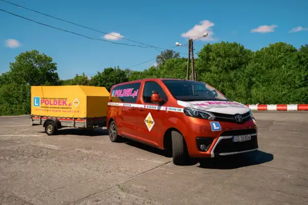 Pomarańczowy bus i żółta przyczepa z logo "POLDEK.pl" na placu manewrowym. Dowiedz się, ile kosztuje prawo jazdy E.