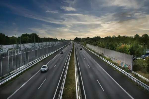 Szeroka autostrada A2 z ruchem samochodowym, otoczona zielenią i ekranami akustycznymi.