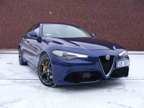 Niebieskie Alfa Romeo Giulia Veloce z żółtymi zaciskami hamulcowymi na tle ceglanej ściany, na śniegu.