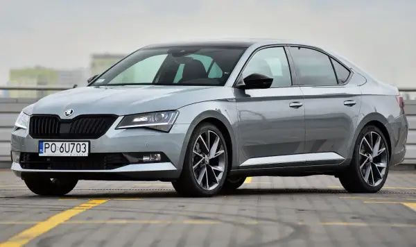 Elegancki, szary Skoda Superb 2024 z czarnym dachem i przyciemnianymi szybami, zaparkowany na parkingu.