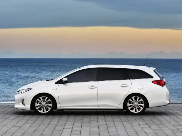 Biała Toyota Auris 1.6 benzyna kombi na tle morza i nieba o zachodzie słońca.